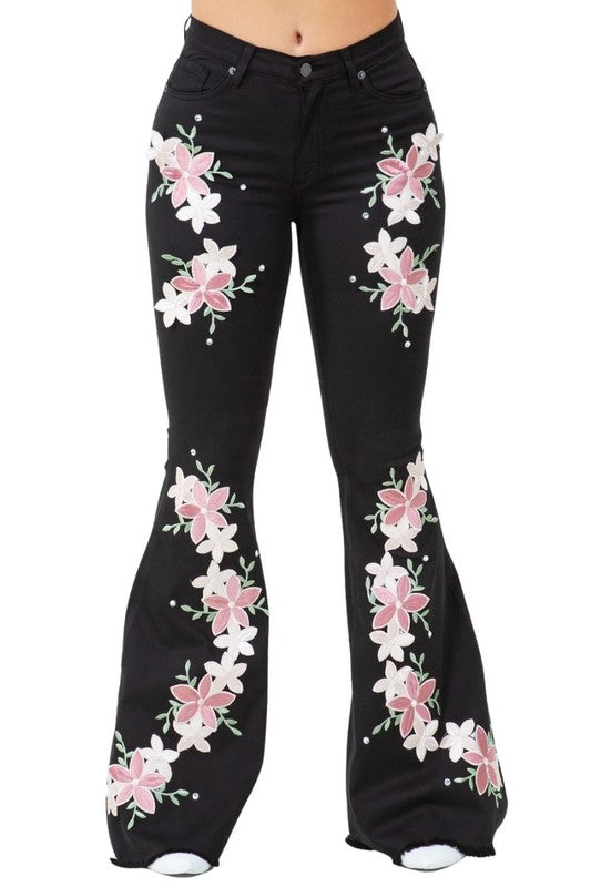 Black bell-bottom jeans with pink and white floral embroidery across the legs