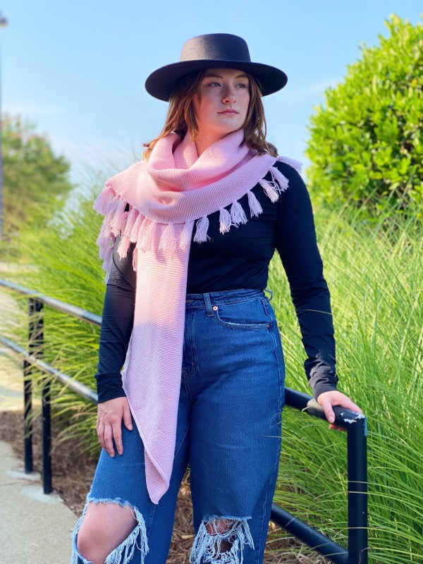 Pink blanket scarf with chunky knit texture and fringe trim, worn lengthwise