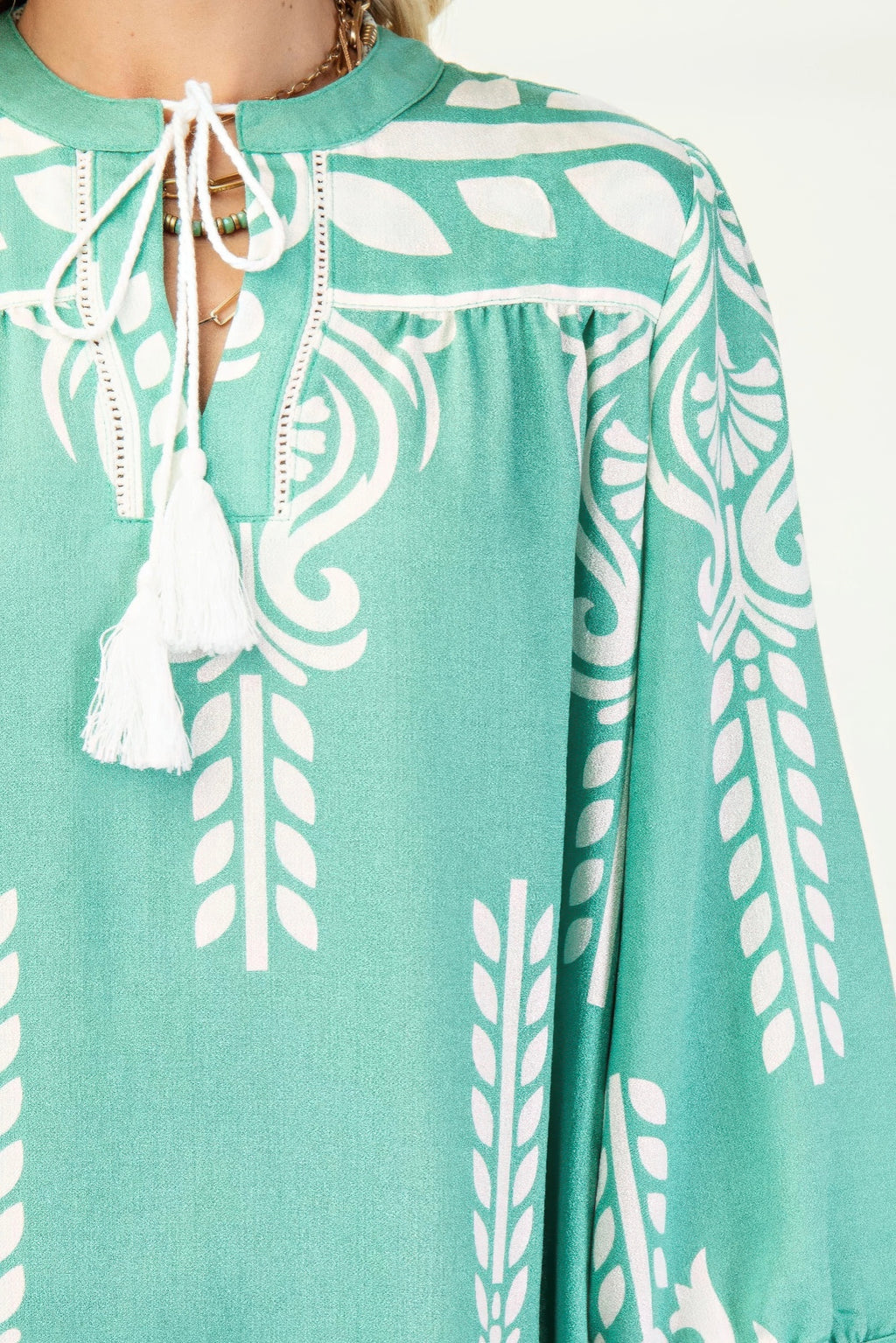 Nahaufnahme: Grün-weißes Printkleid mit weißem Kordelband und Quasten am Ausschnitt