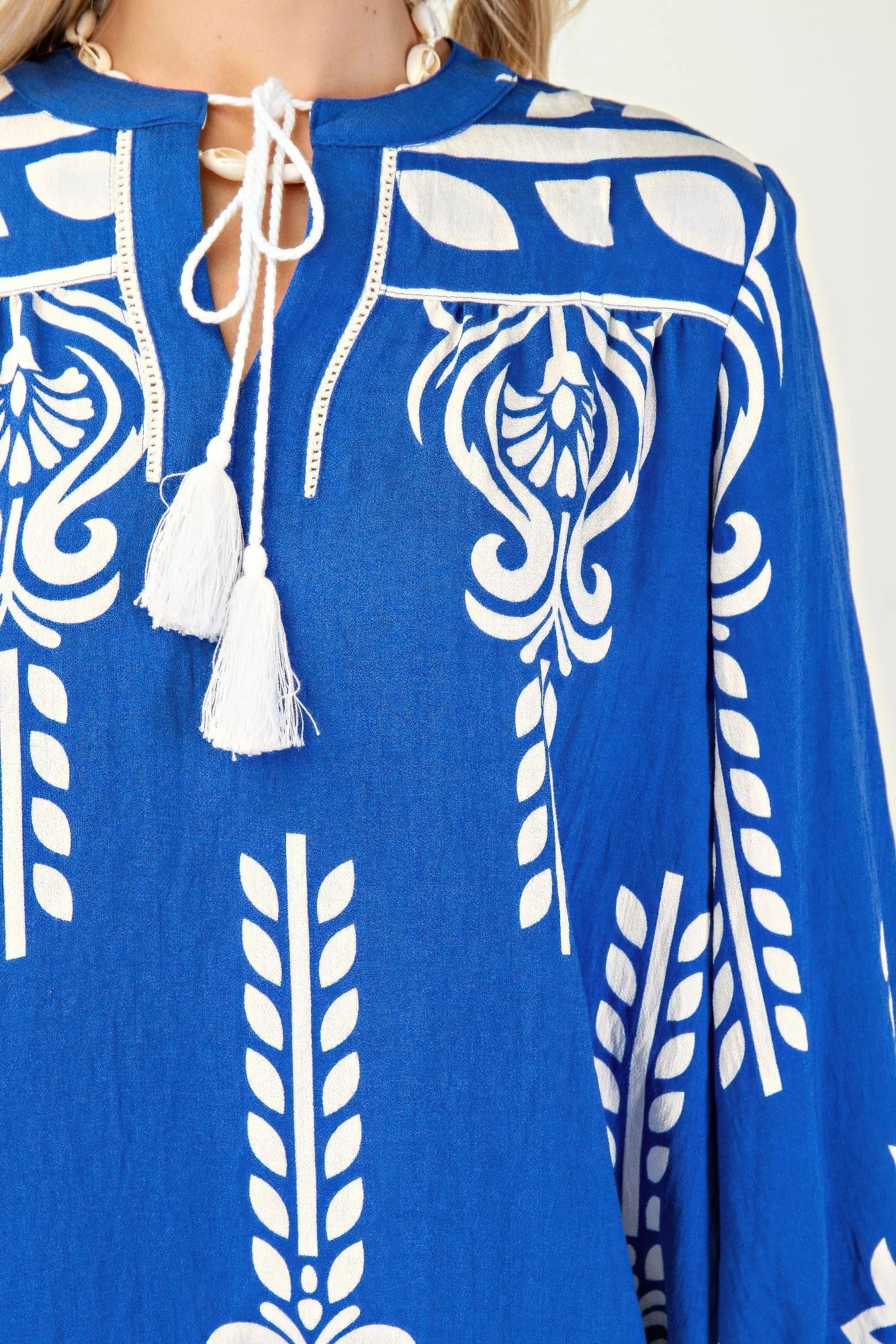 Nahaufnahme: Blaues Kleid mit weißem Ornamentprint, Kordelband mit Quasten am Ausschnitt