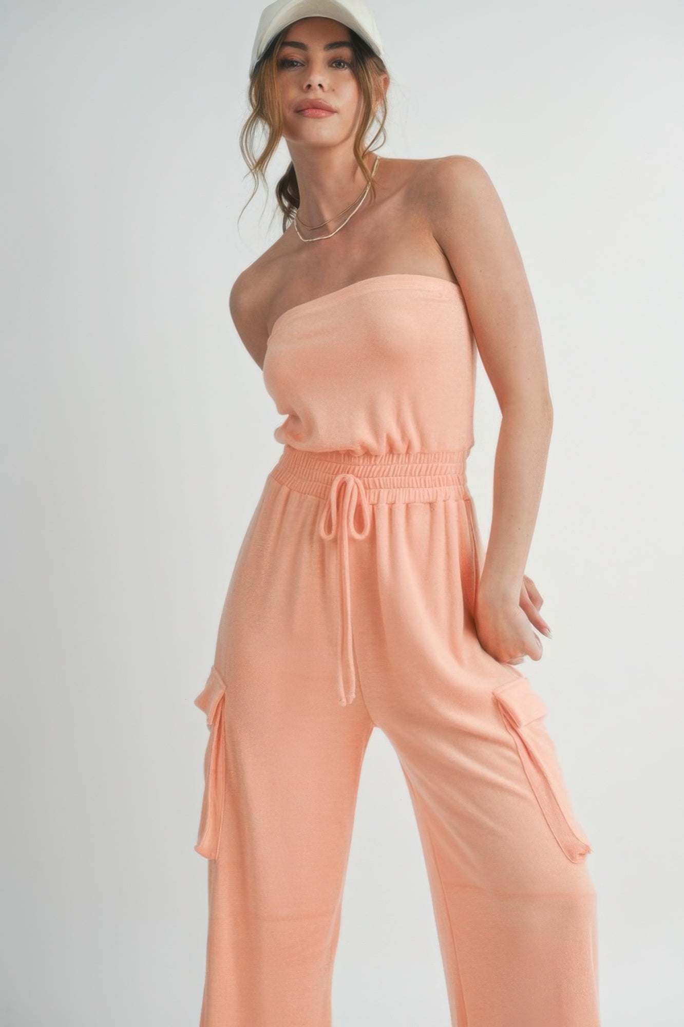 Peach tube top jumpsuit front view with elastic smocked waist and cargo-style side pockets