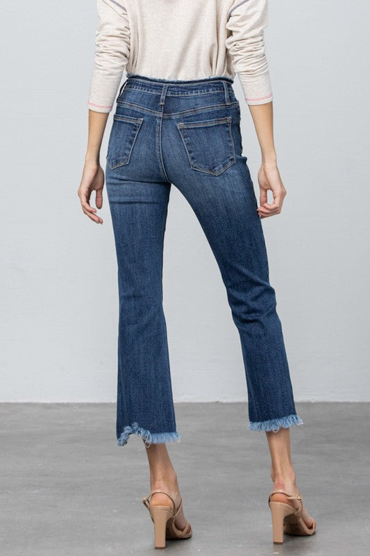 Dark blue bootcut crop jeans close-up: five-pocket front and raw frayed hem