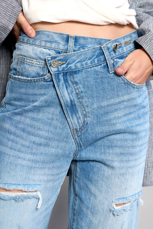 Close-up of high-waist crossover waistband and button on medium wash ripped straight jeans.
