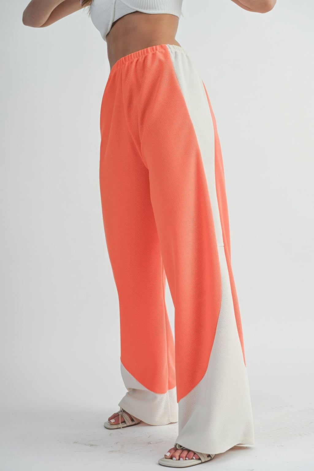 Side view: coral wide-leg pants with long curved light panel and elastic waistband.