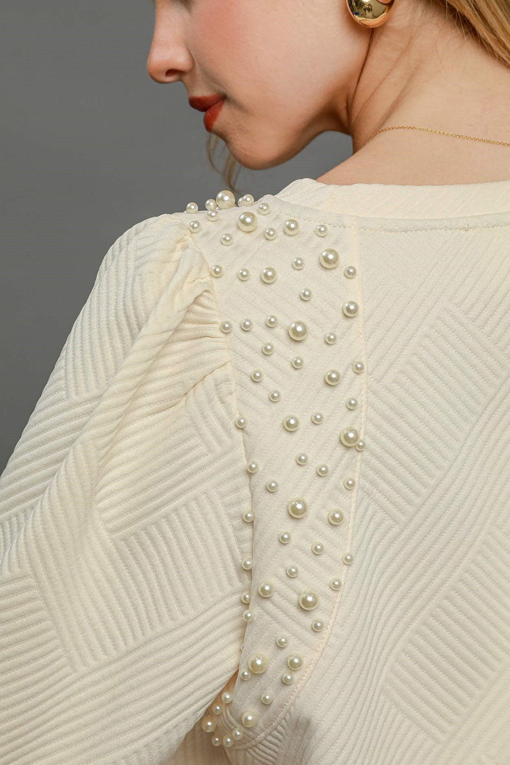 Cream knit top close-up: pearl beading on textured puff sleeves and shoulders