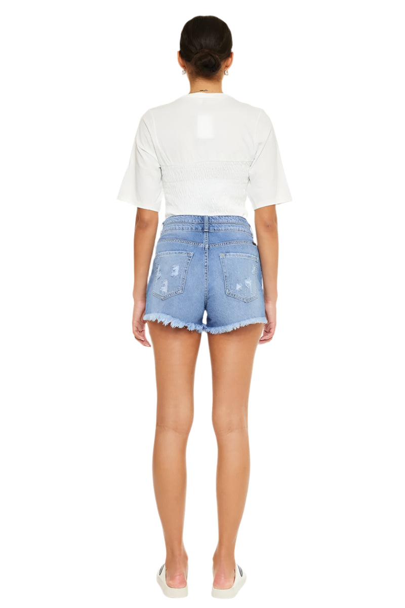 Back view of high-rise blue denim jean shorts with patch pockets and frayed hem