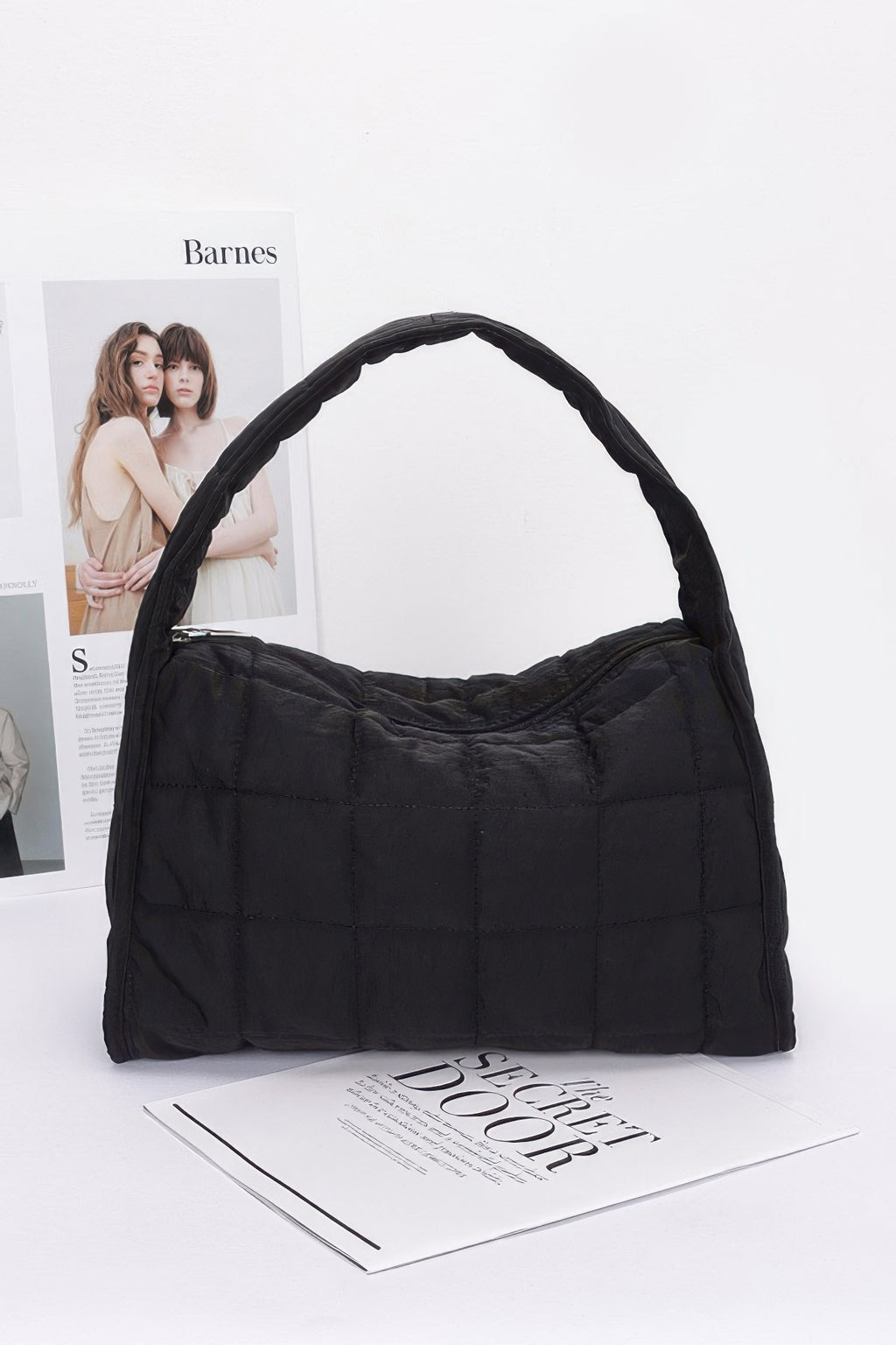 Black quilted nylon shoulder bag with curved handle and stitched quilted panels