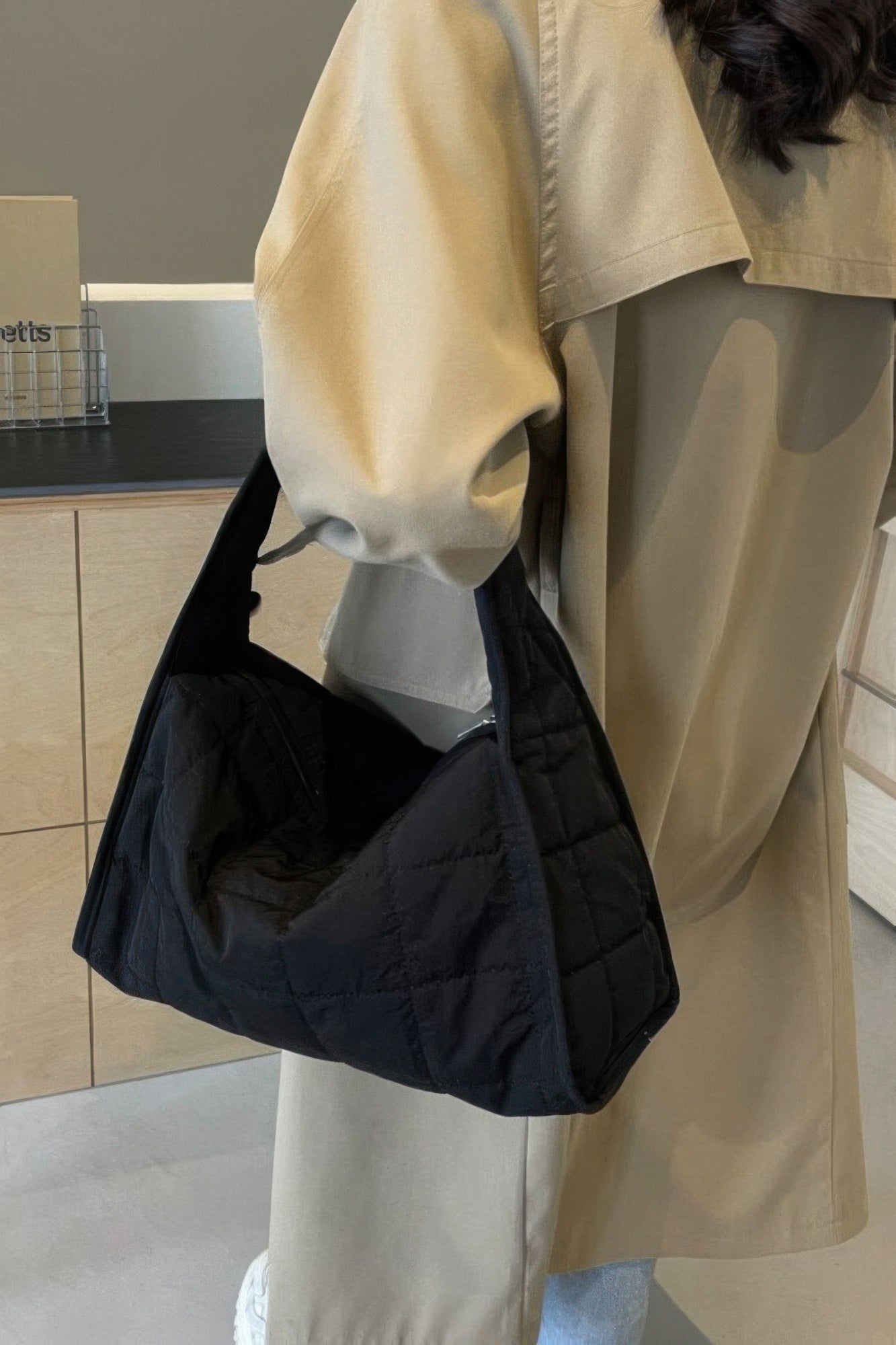 Black quilted nylon shoulder bag on shoulder with triangular quilted body