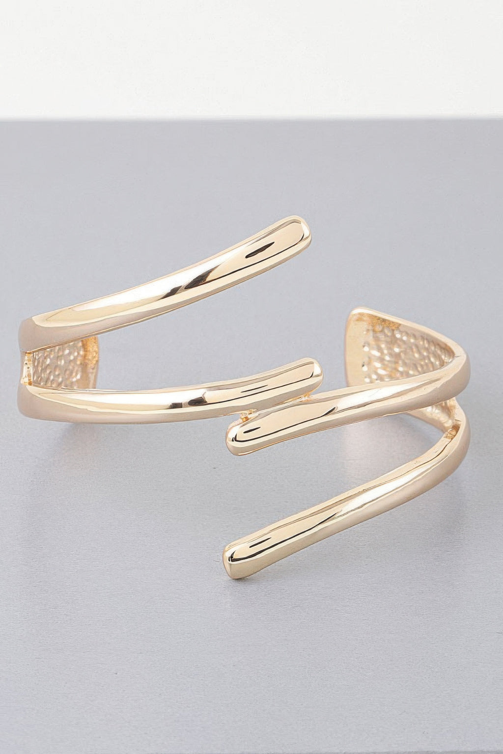 Gold open cuff bracelet with curved triple-bar design and textured inner details