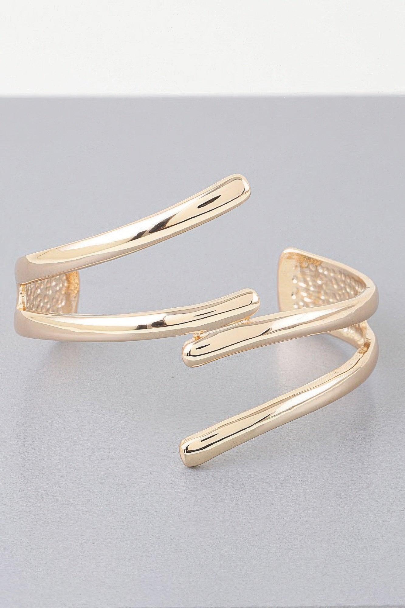 Gold open cuff bracelet with curved triple-bar design and textured inner details