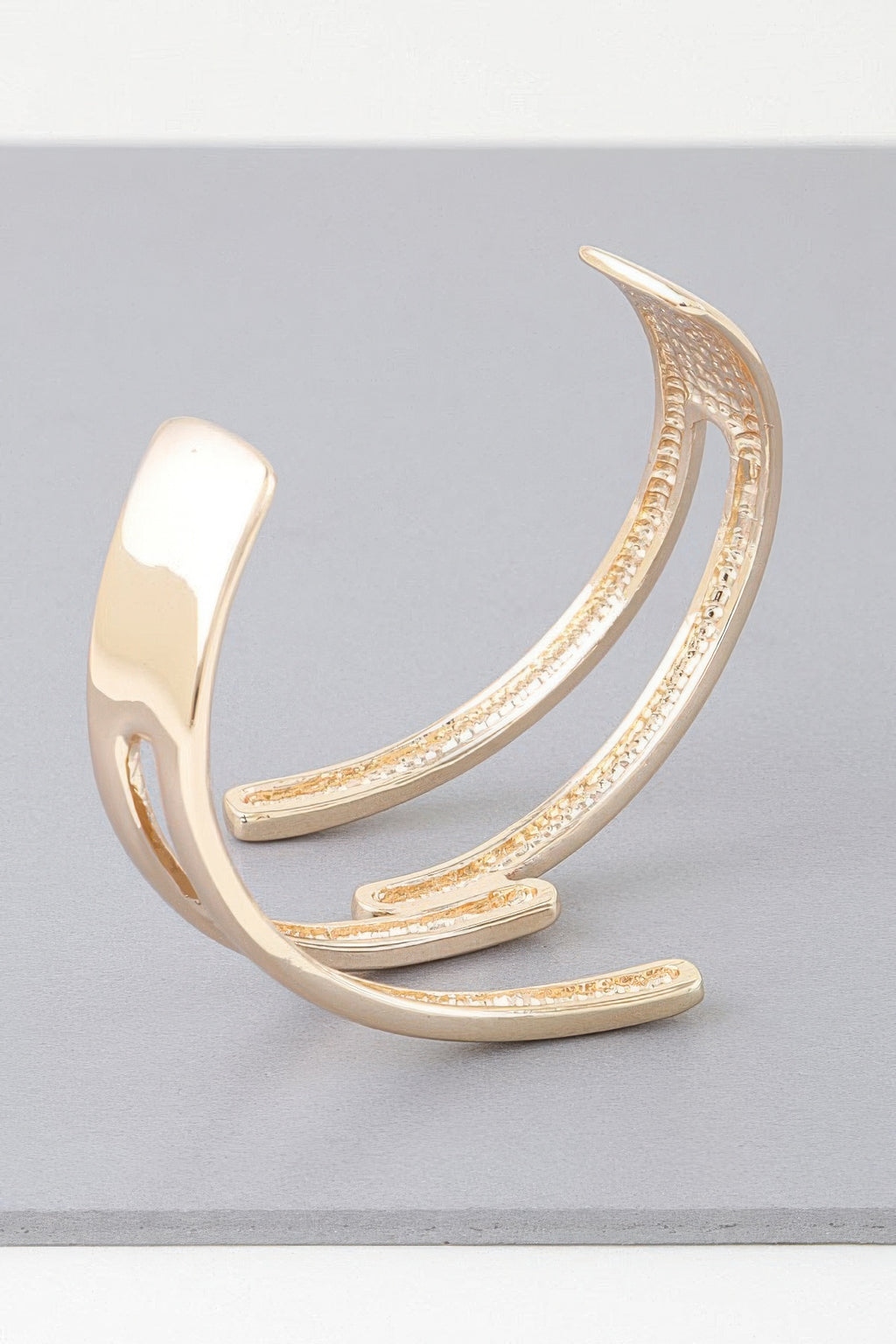 Delicate gold cuff bracelet with raised curved bars and sparkling textured accents