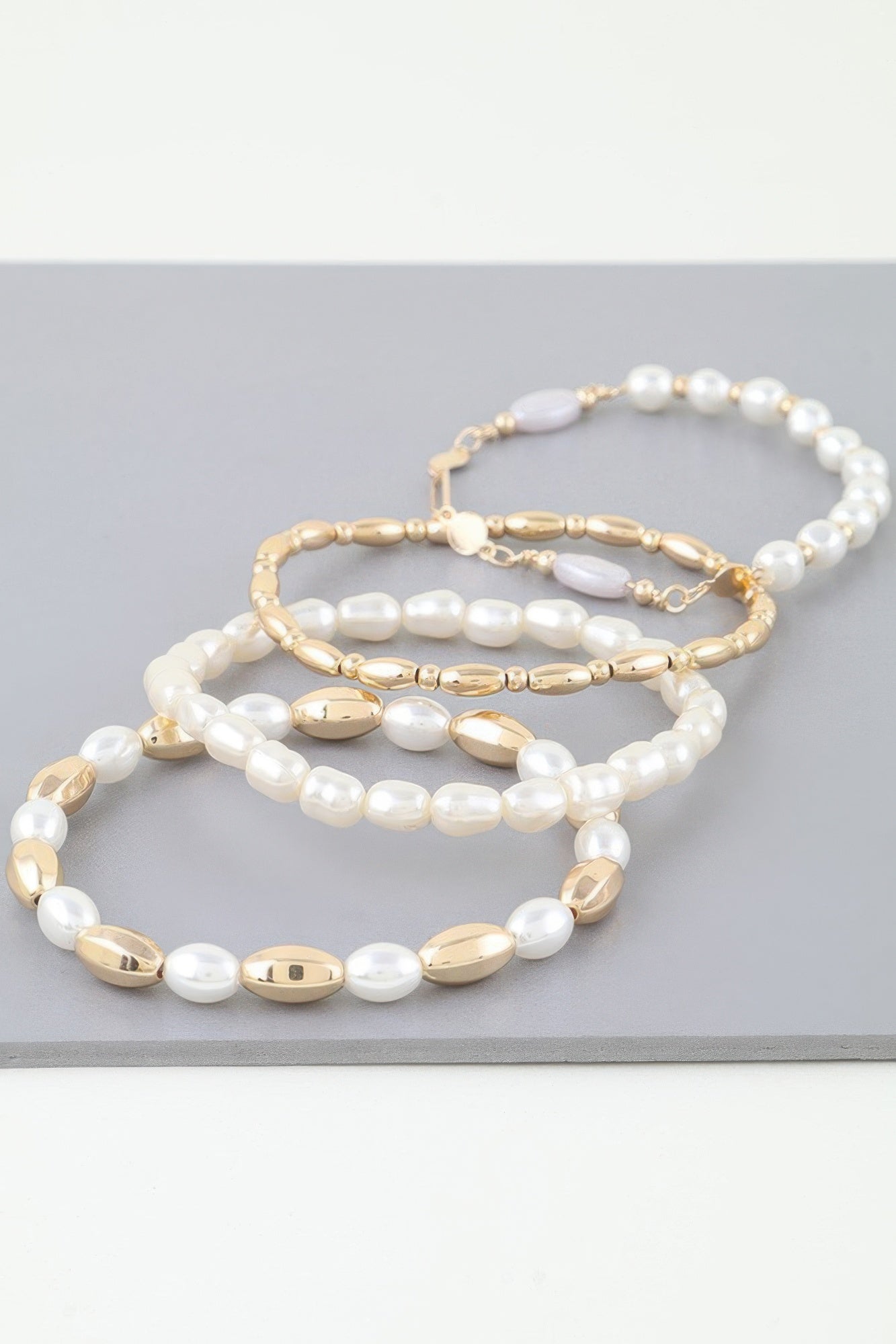 Gold and cream pearl beaded bracelet stack with oval metal accents and strands
