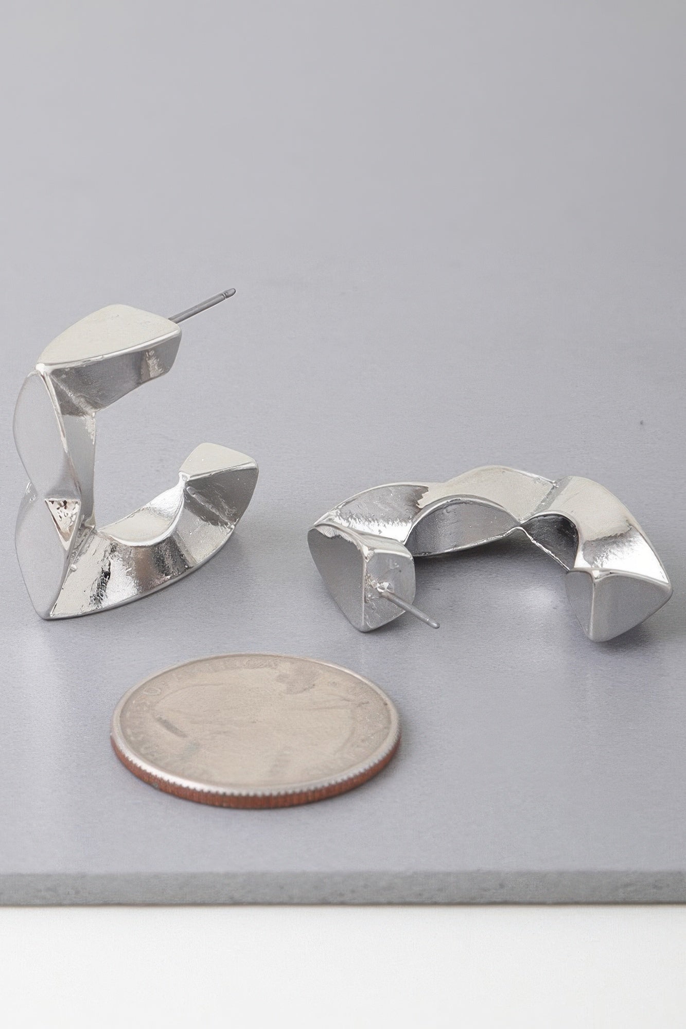 Silver geometric cubic hoop earrings with faceted open arches and stud posts.