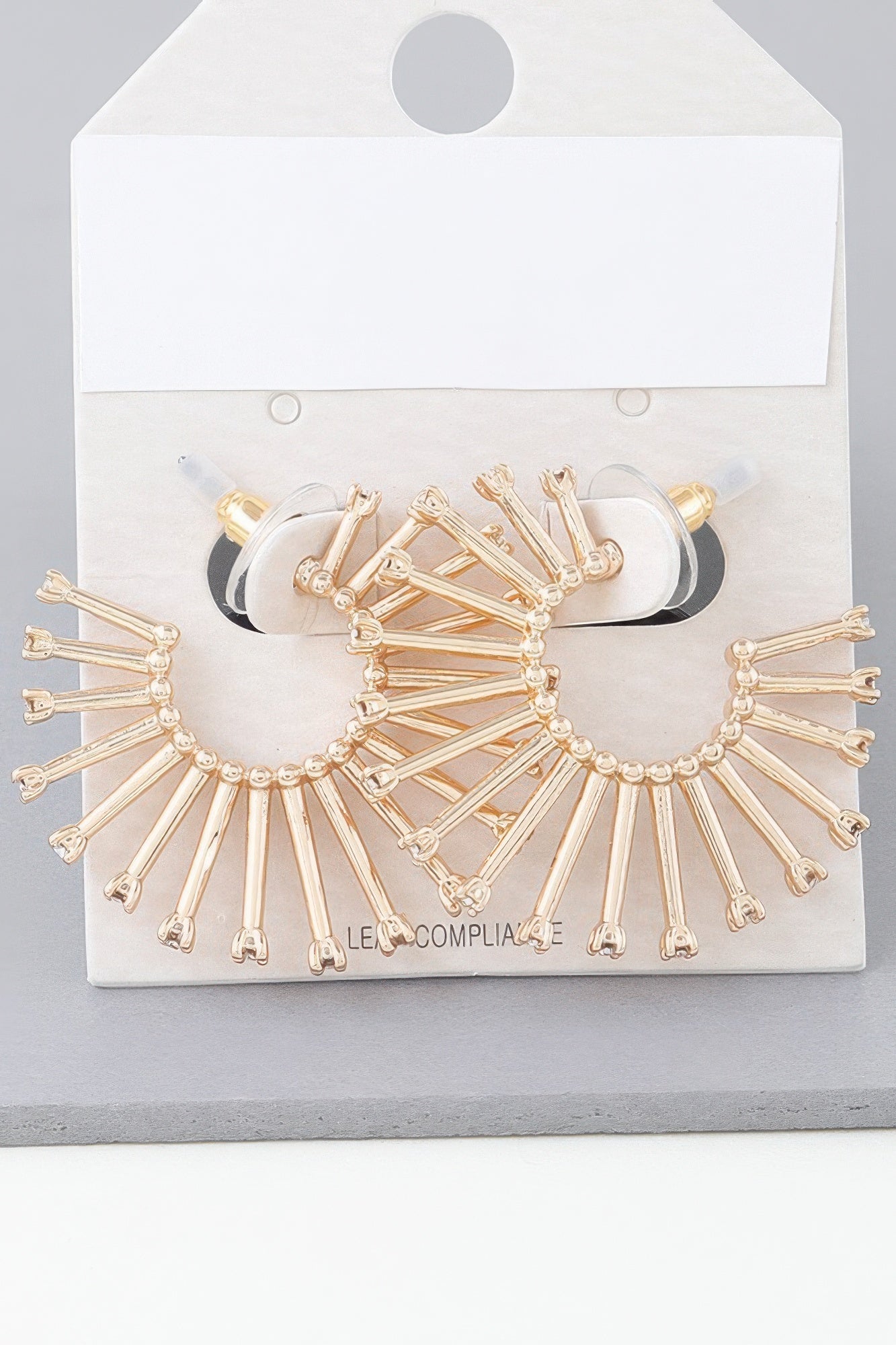 Gold-tone sun hoop earrings with radiating bars and clear stones on display card