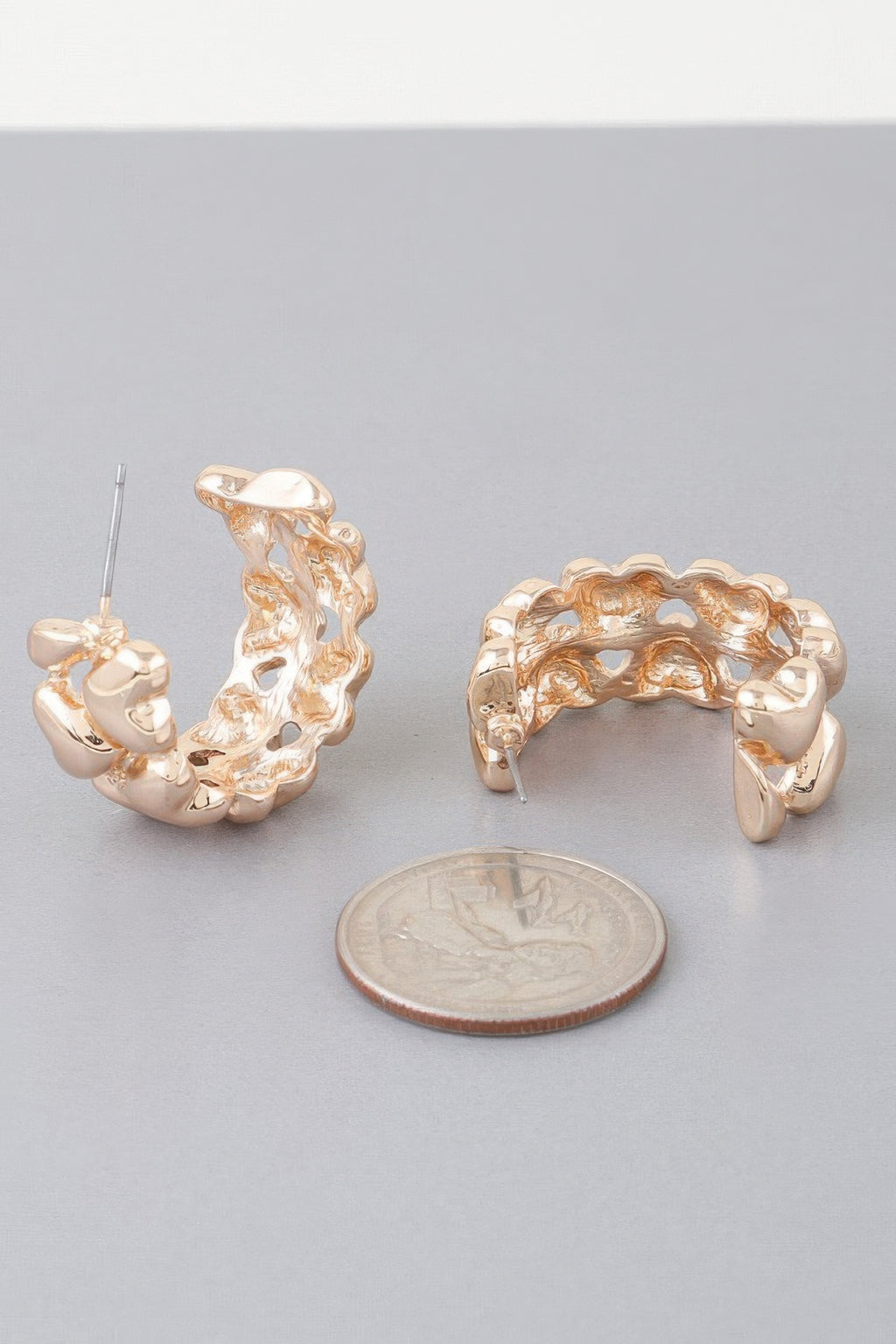 Gold twin-heart hoop earring with wire post; close view beside coin for scale