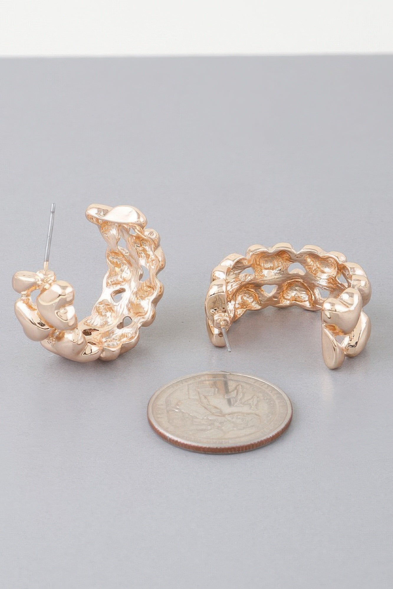 Gold twin-heart hoop earring with wire post; close view beside coin for scale