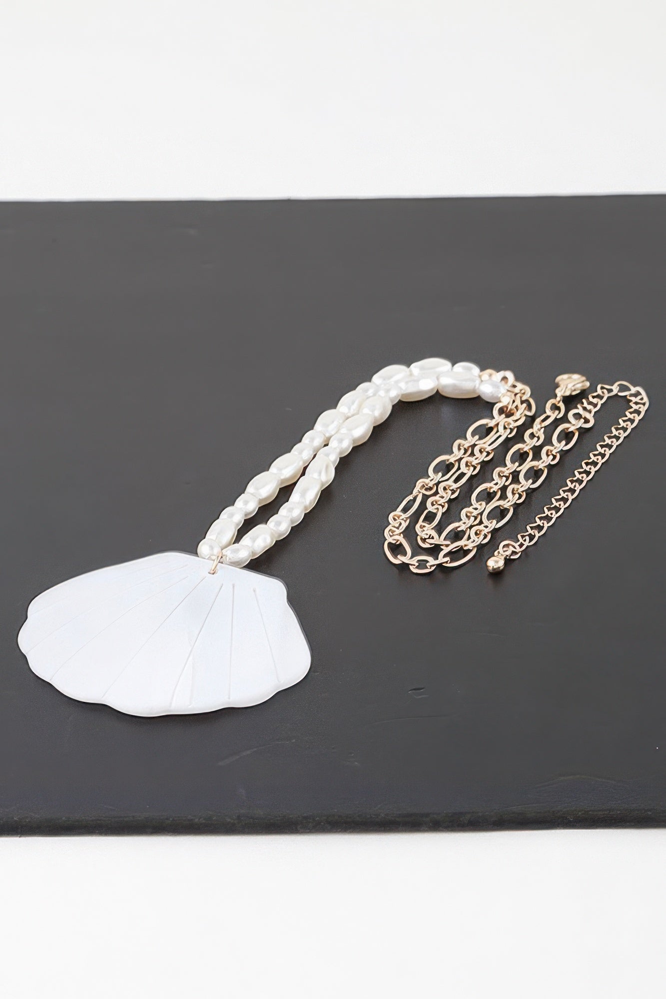 Seashell bead necklace laid flat: white shell pendant, pearl beads, gold-tone chain