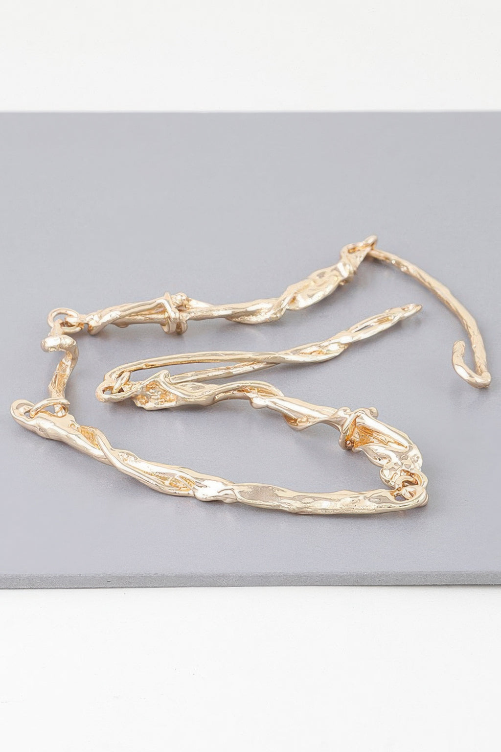 Gold multi-twisted abstract necklace laying flat, textured curved links and clasp