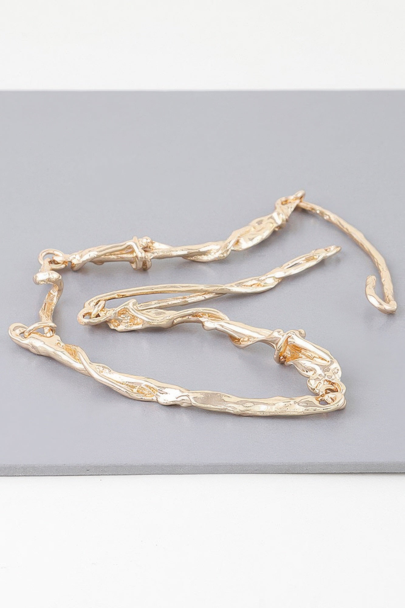 Gold multi-twisted abstract necklace laying flat, textured curved links and clasp
