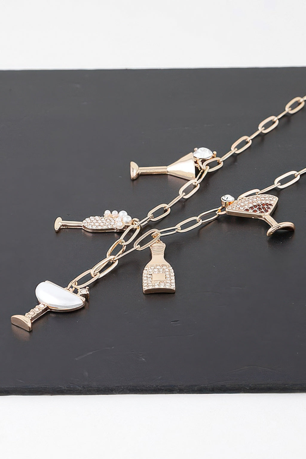 Gold-clear drinks charm necklace, laid flat: martini, bottle, and glass pendants