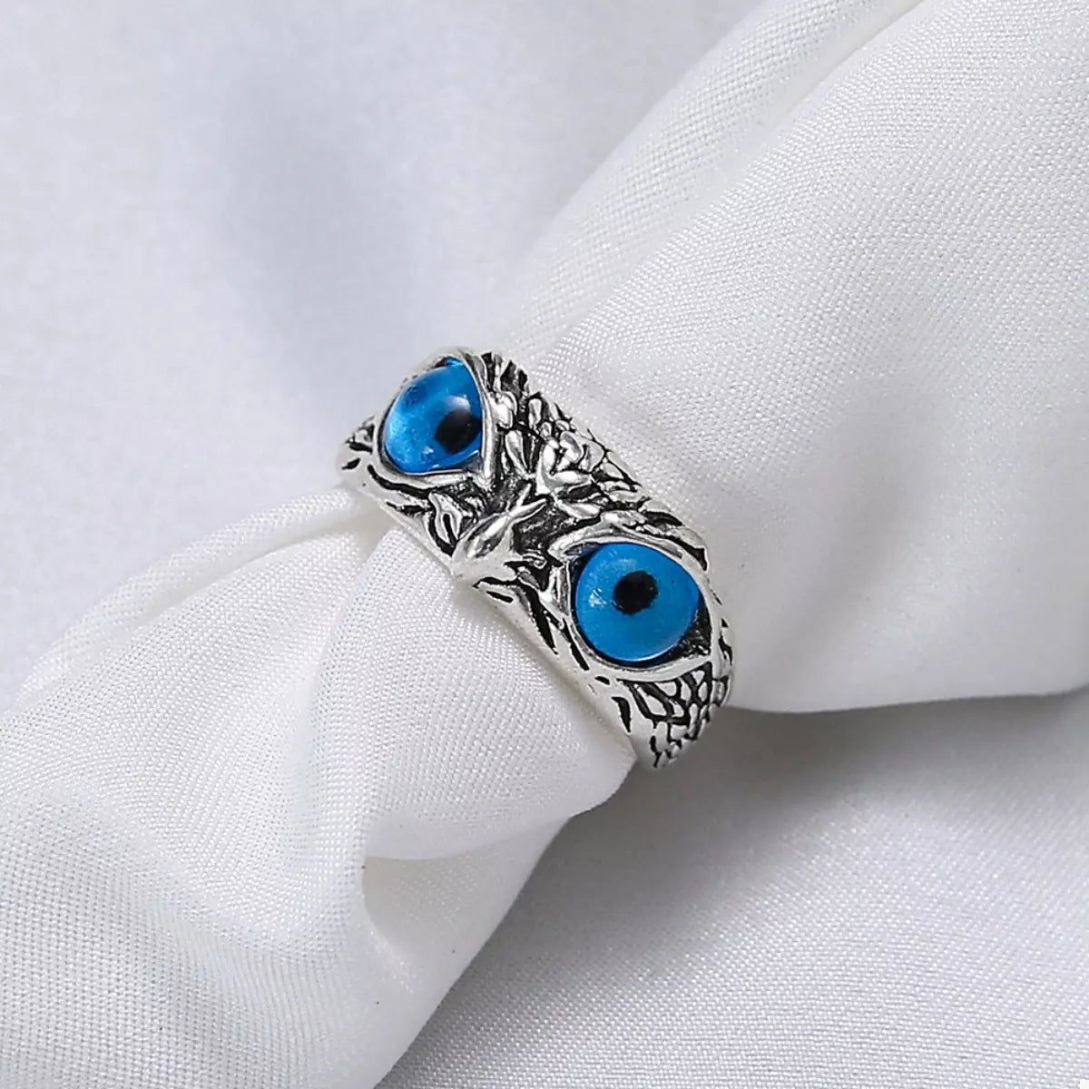 Silver owl eyes ring on folded fabric, two blue eye cabochons and engraved pattern