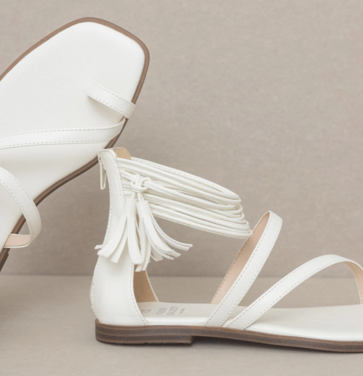 Close-up of white ankle wrap sandal with tassel fringe and double front straps