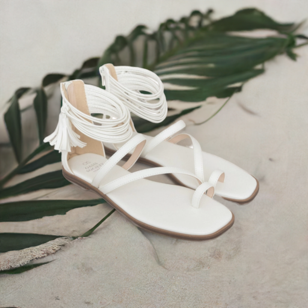 White thong-style sandals with ankle wrap, tassel fringe, and flat tan sole