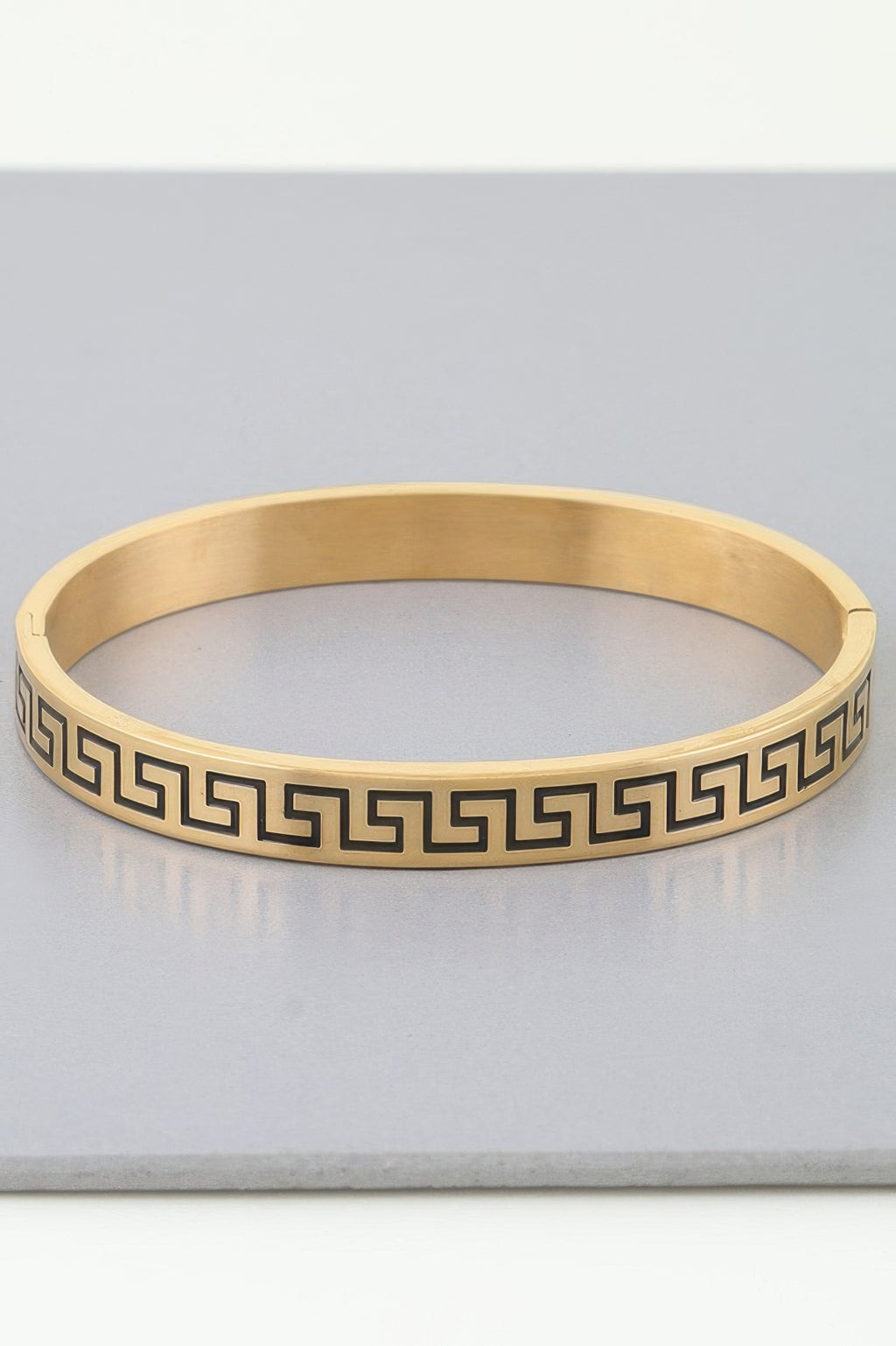 Gold cuff bracelet with repeating maze/Greek-key pattern around the band