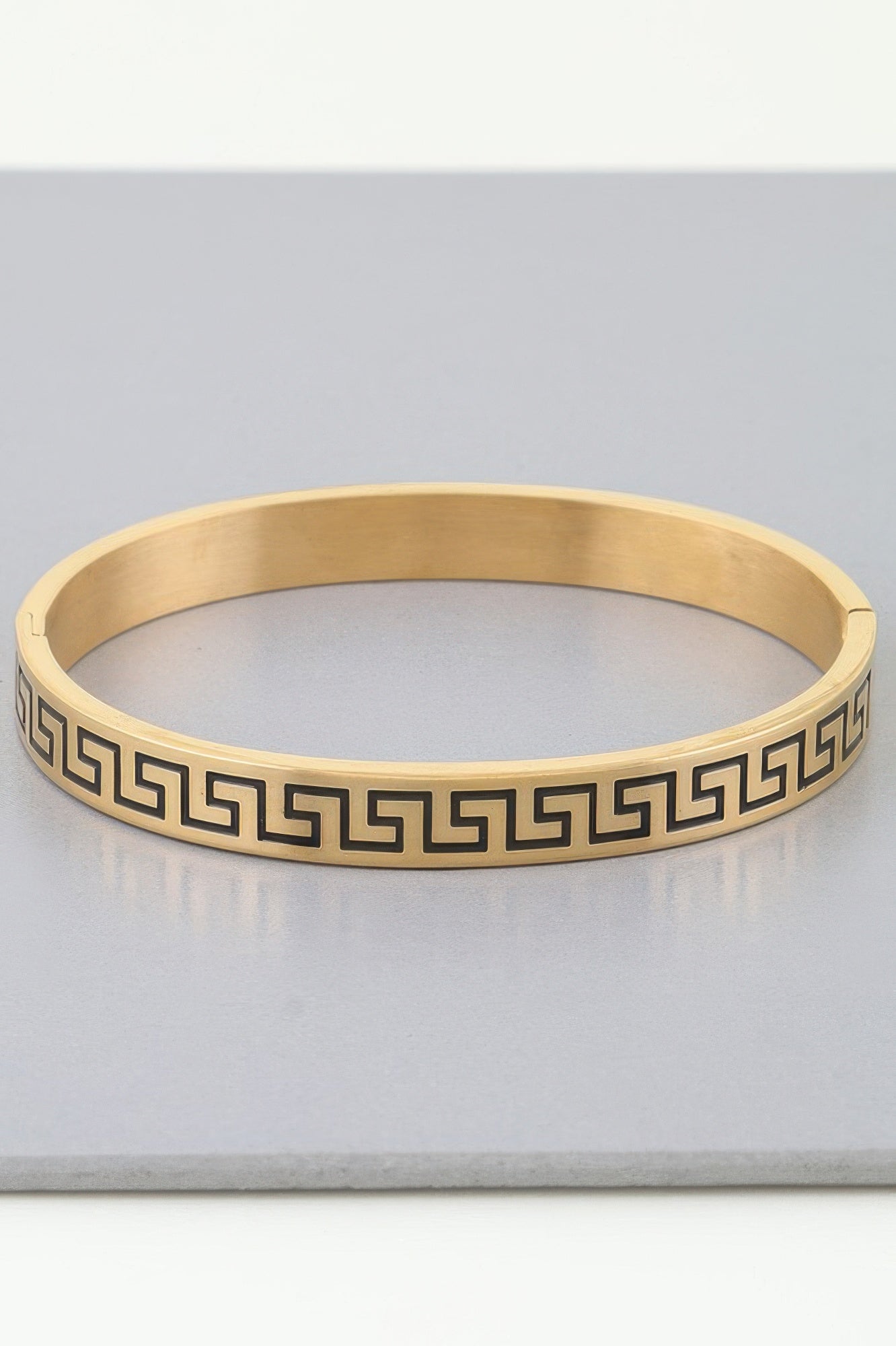 Gold cuff bracelet with repeating maze/Greek-key pattern around the band