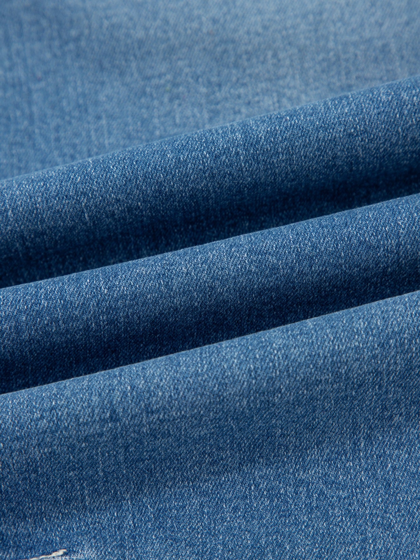 Medium-wash denim fabric texture on washed barrel jeans with twill weave