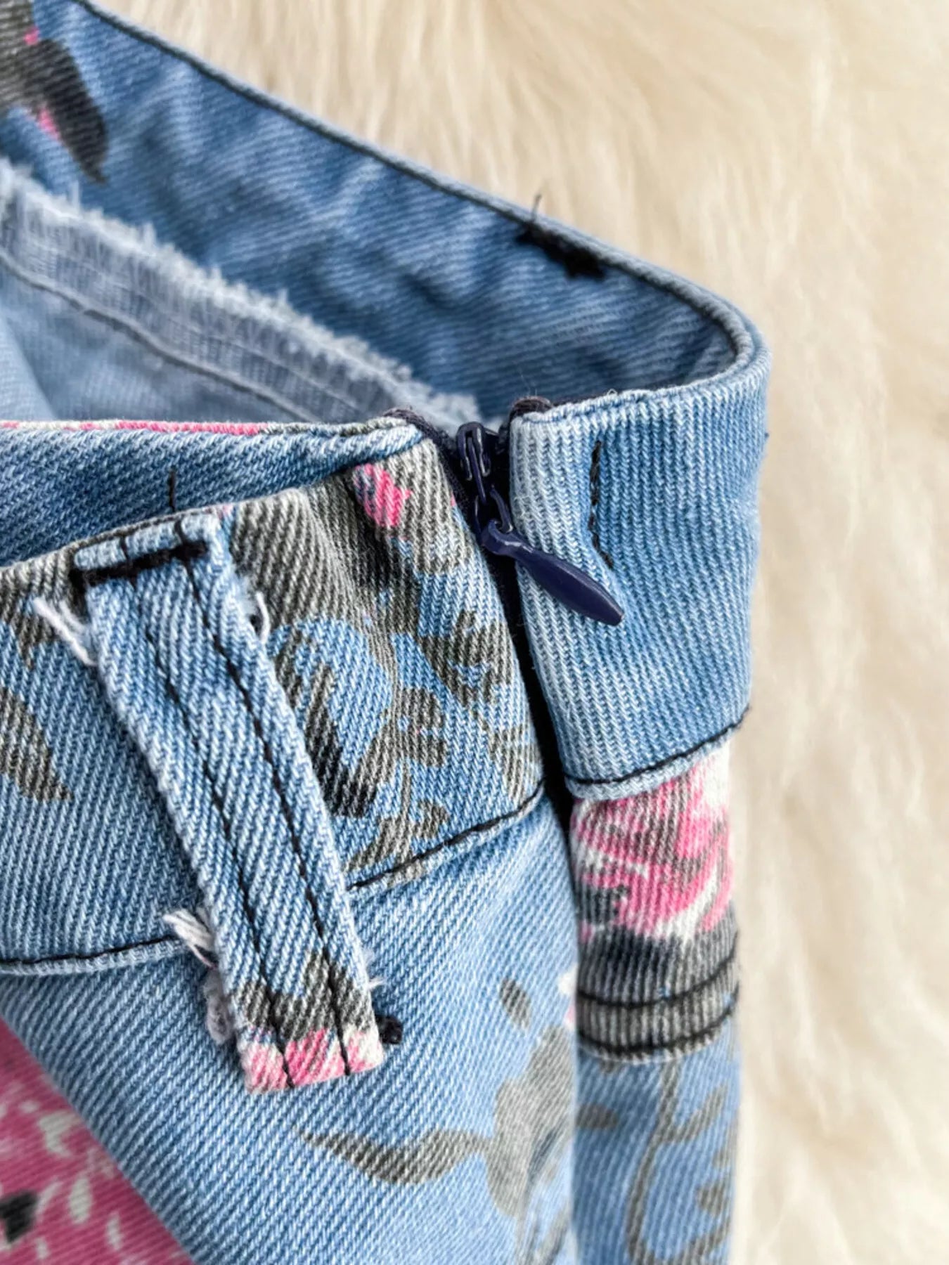 Denim skirt waistband detail with visible zipper and floral print pocket panel