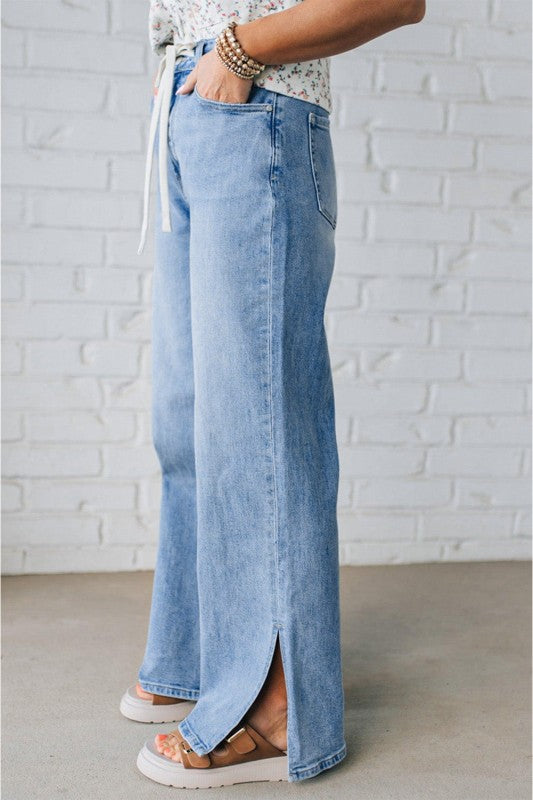 Light blue jeans with front drawstring and high-rise waistband, side slit hem.