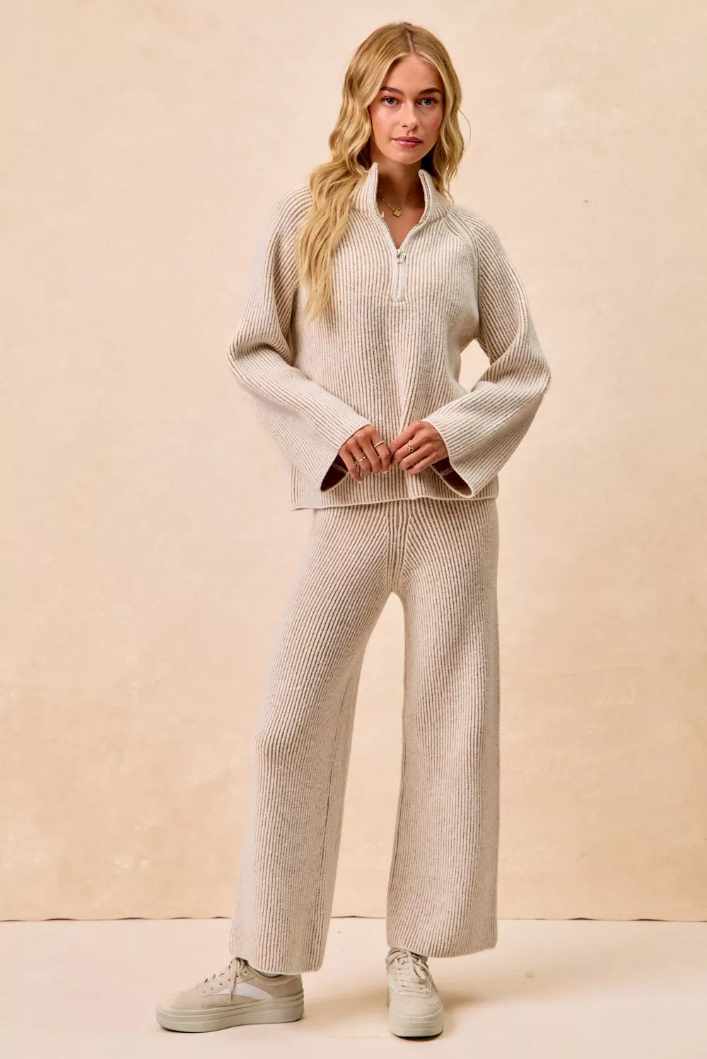 Taupe two-tone ribbed knit top with stand collar half-zip, hands clasped