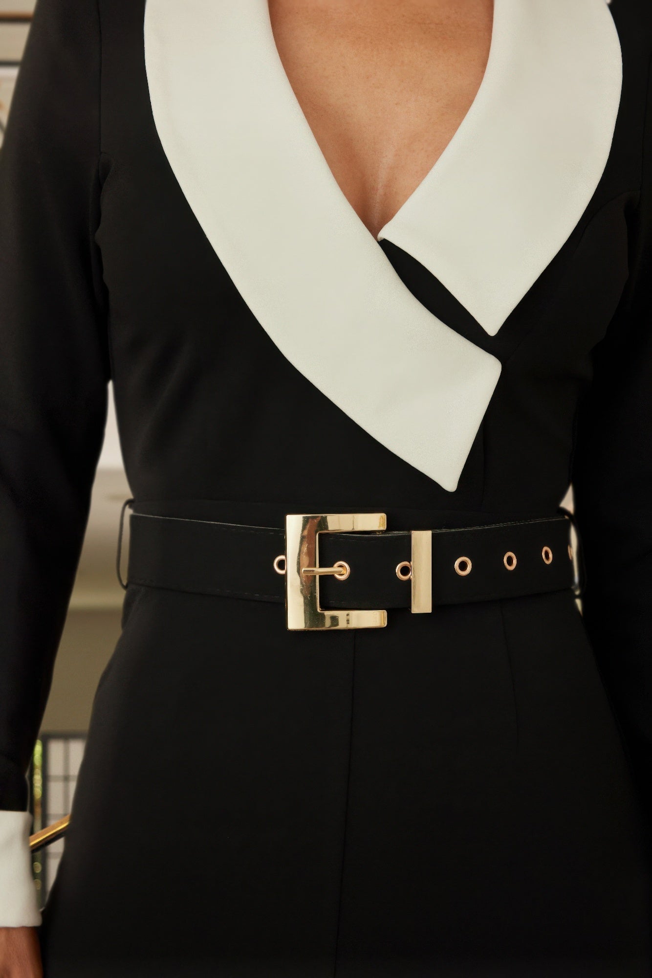 Close-up: black jumpsuit waist belt with gold buckle and eyelets over white V-collar
