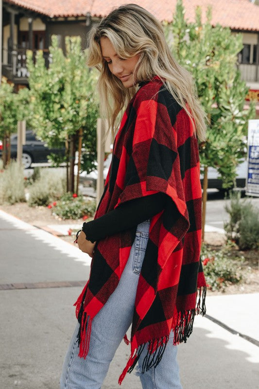 Red-and-black buffalo check tassel poncho with fringe along the hem