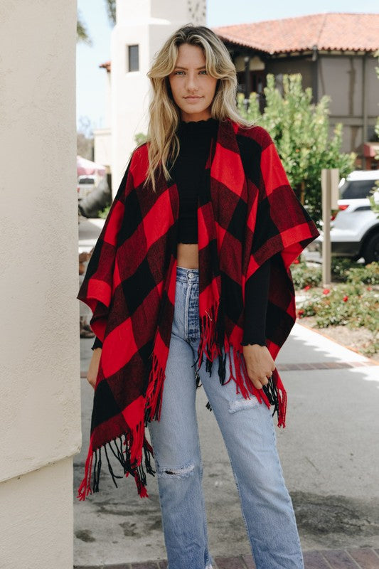 Red-and-black plaid poncho with tassels, draped over jeans and top layer