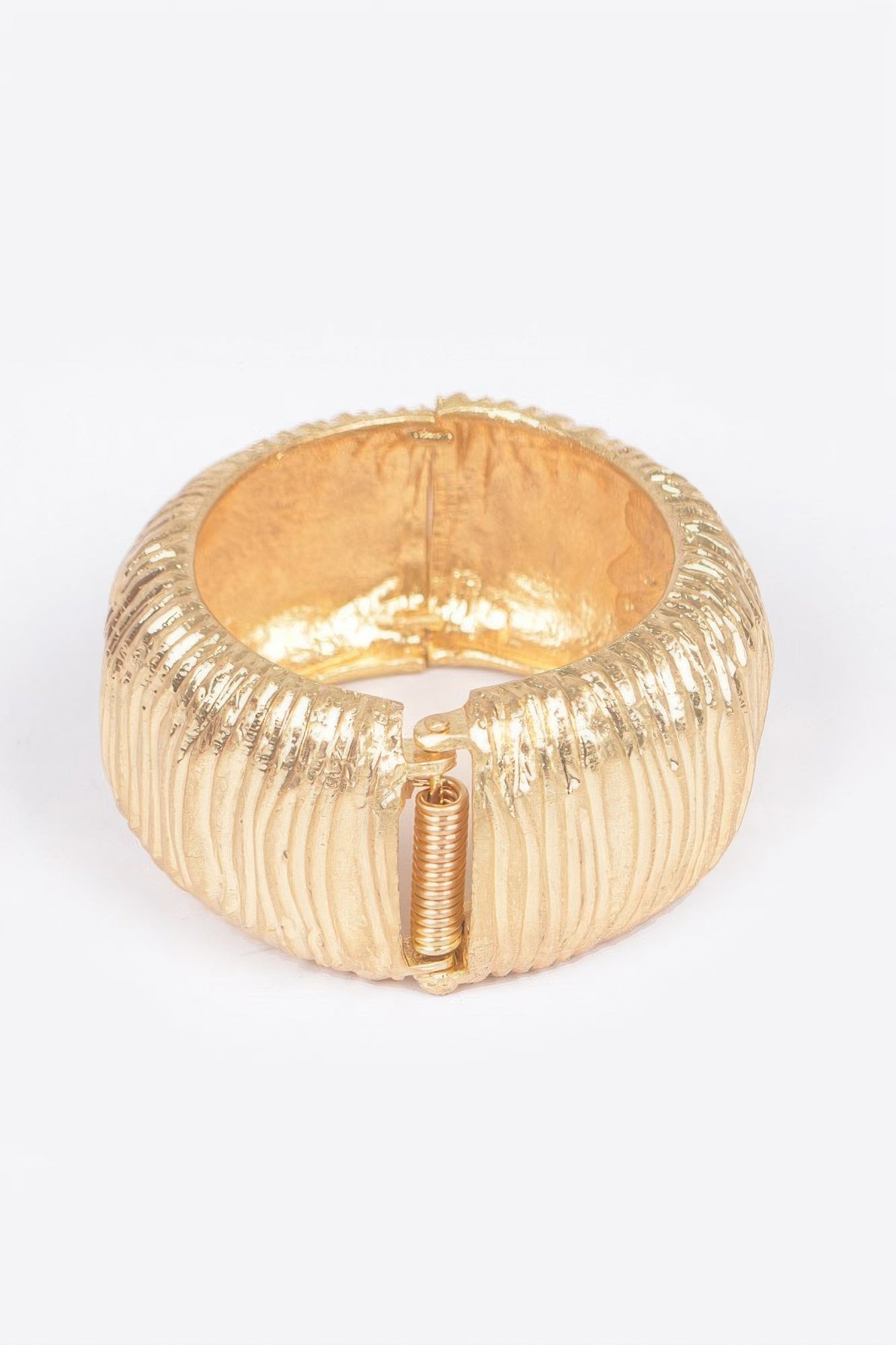 Gold spring hinge cuff bracelet with visible coil spring and ridged band