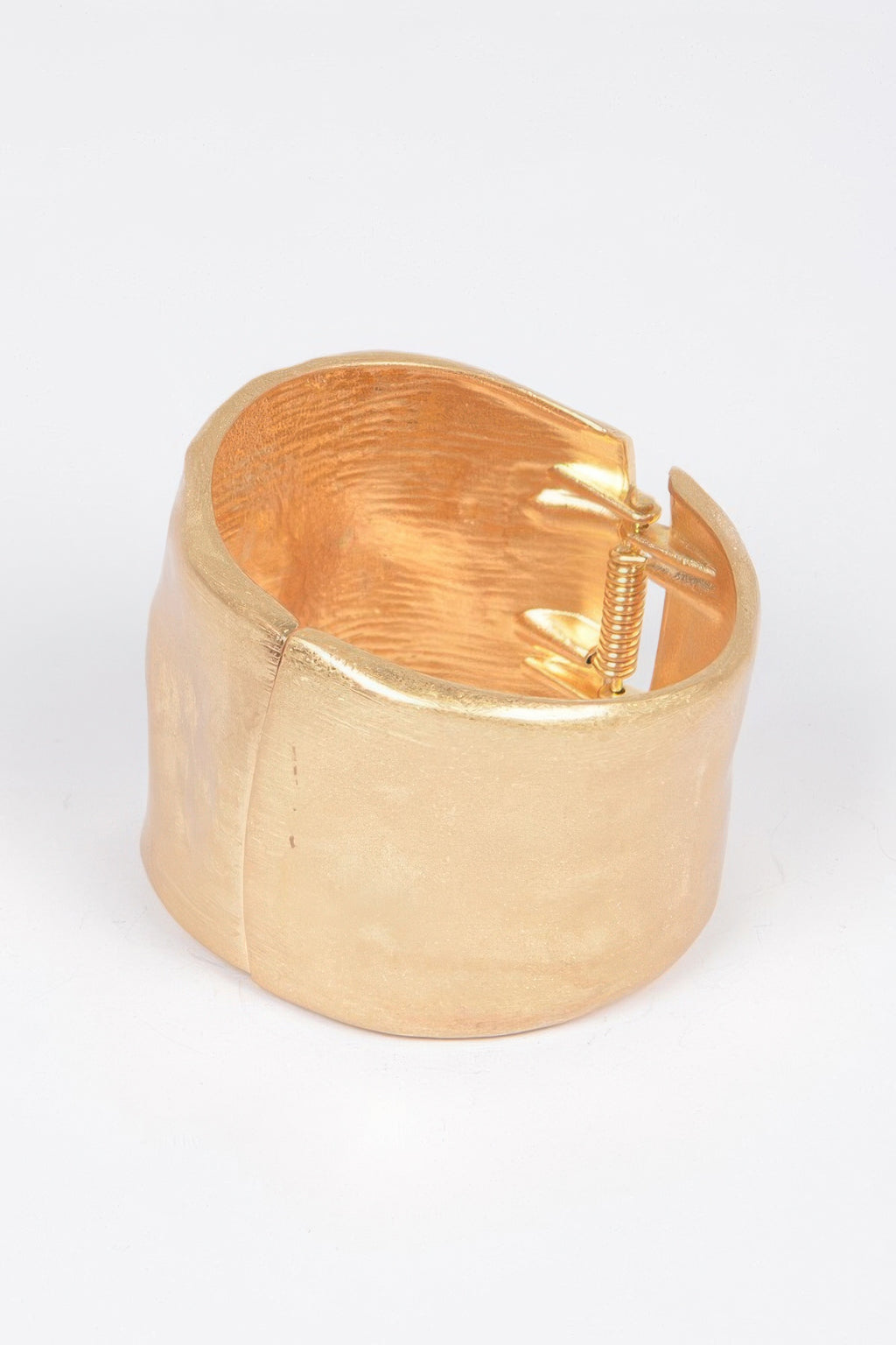 Gold cast cuff bracelet open with spring mechanism visible inside