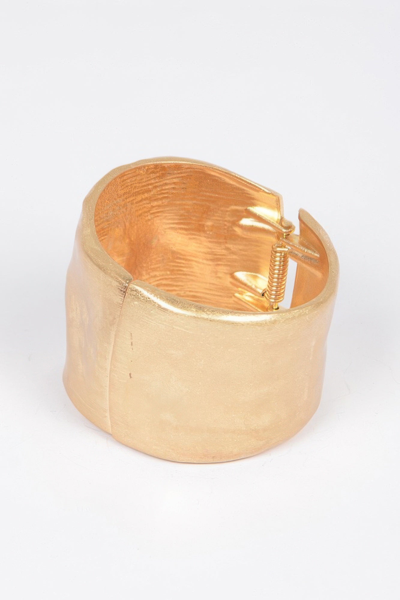 Gold cast cuff bracelet open with spring mechanism visible inside