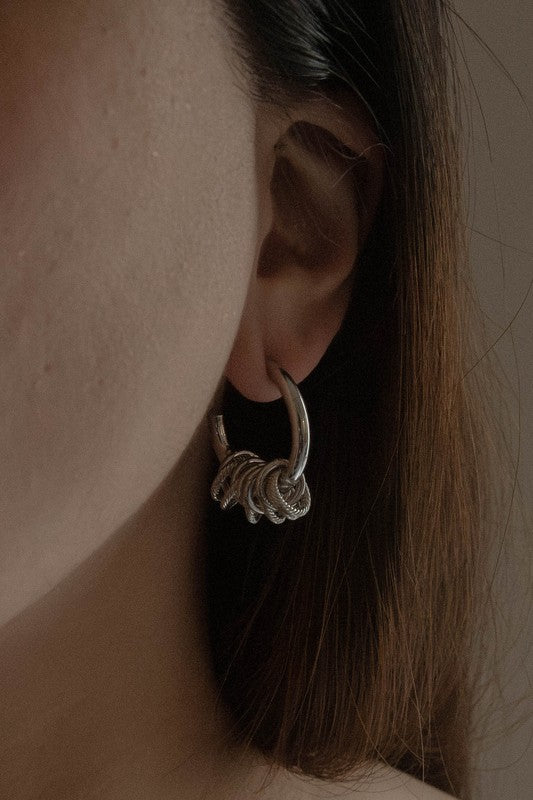Silver hoop earrings worn on ear, chunky linked knotted charm detail
