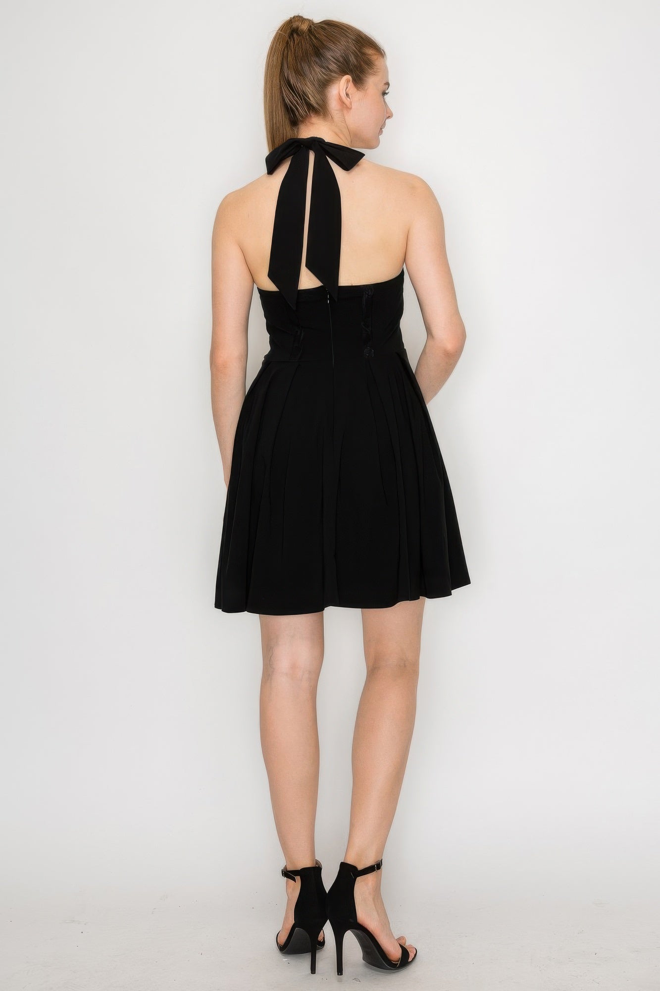 Back view of black corset-style dress with self-tie ribbon halter straps and pleats