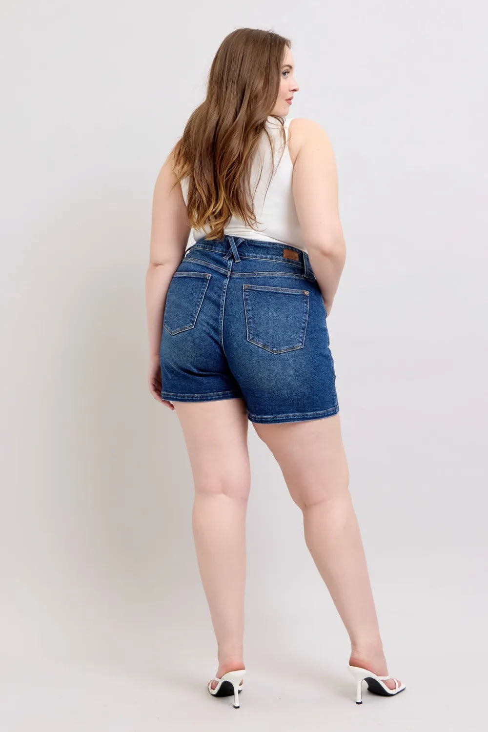 Dark denim plus-size shorts with belted waist and button closure, side view