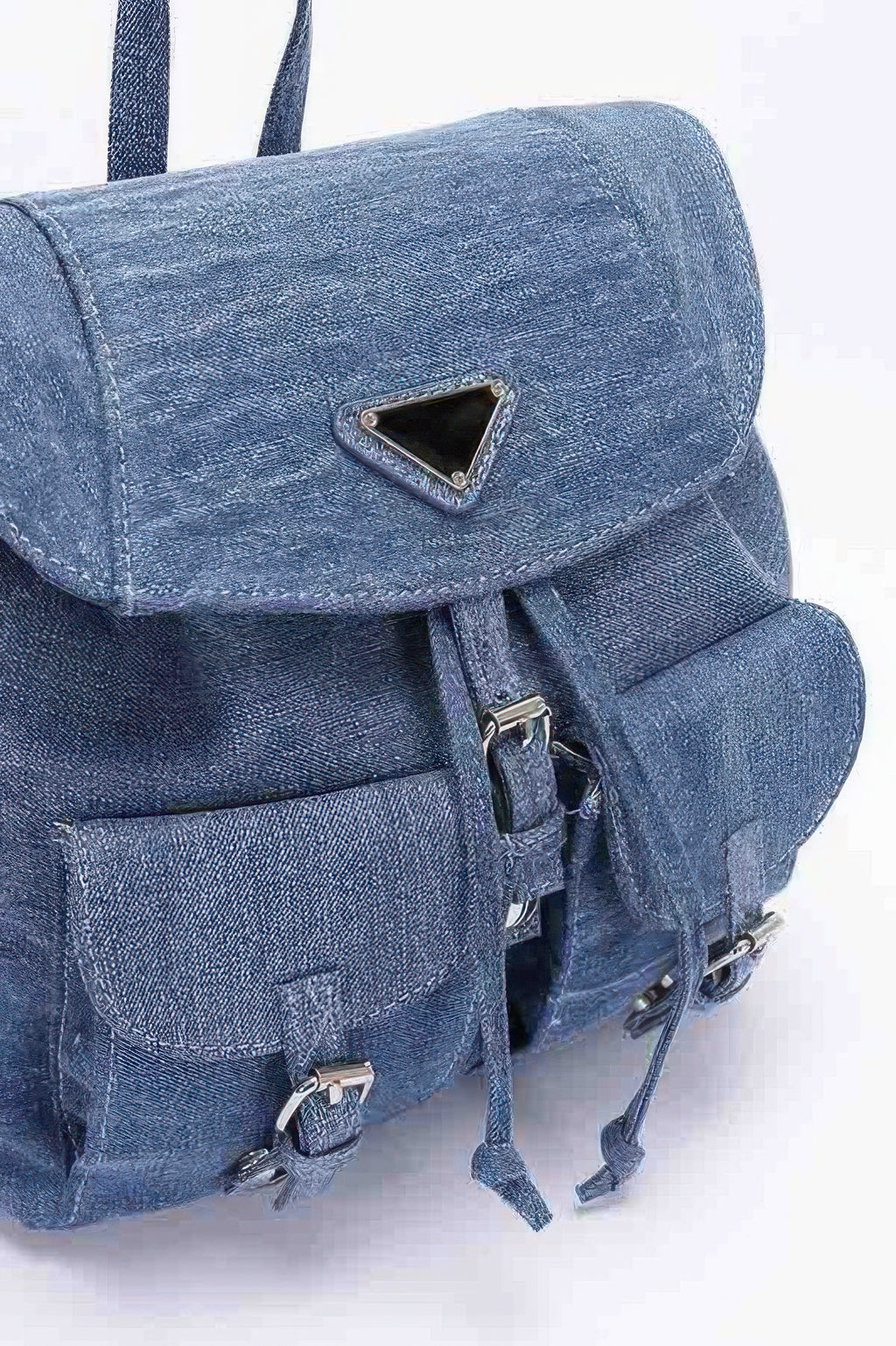 Close-up: denim backpack flap with triangular metal patch, zipper pull, front pocket straps