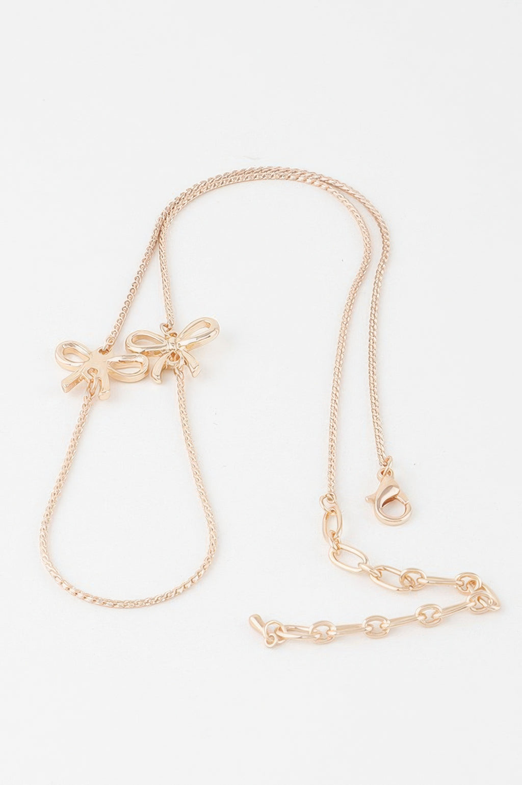 Gold ribbon chain necklace, bow pendant at one end with extender and clasp