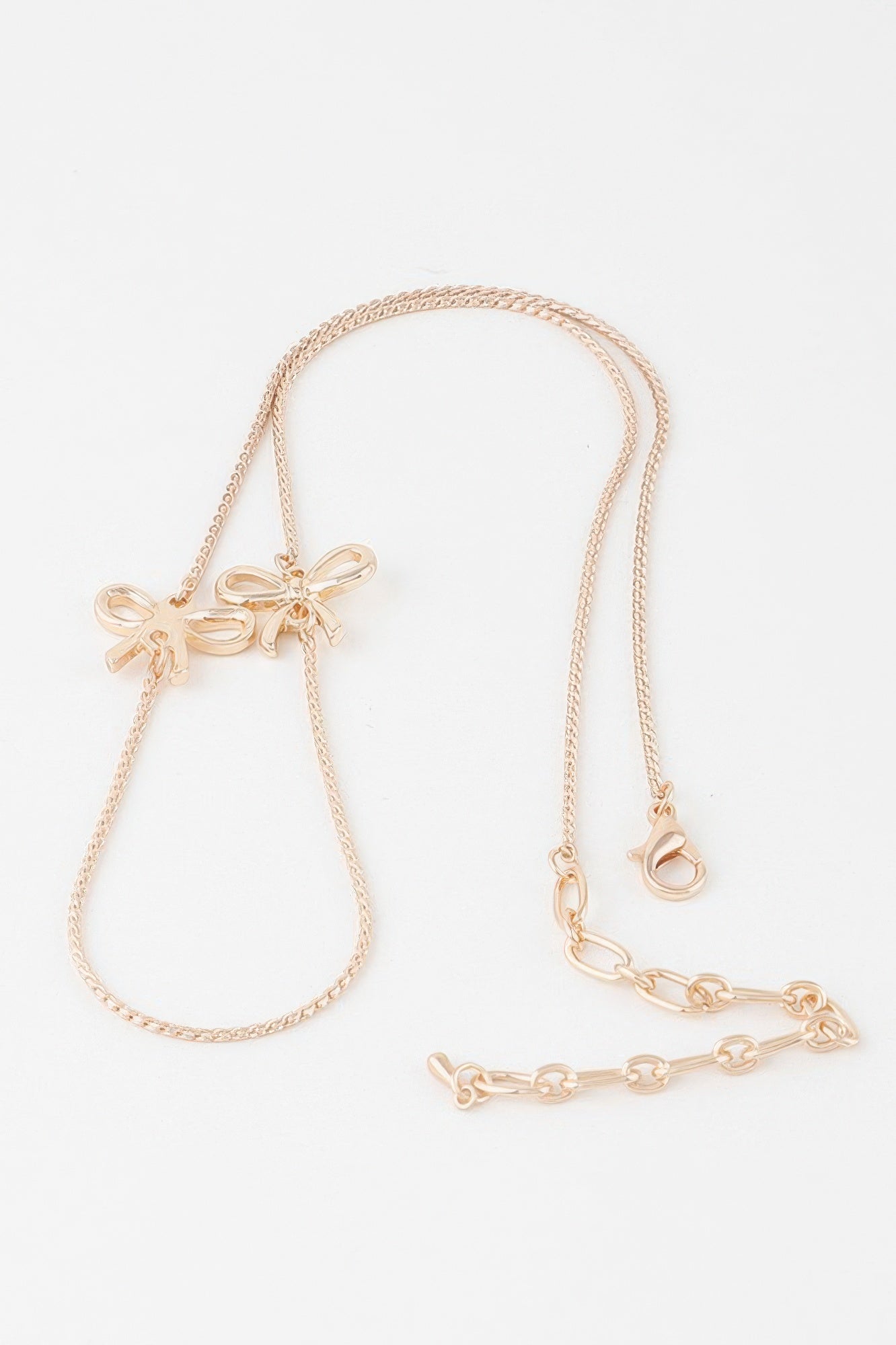 Gold ribbon chain necklace, bow pendant at one end with extender and clasp
