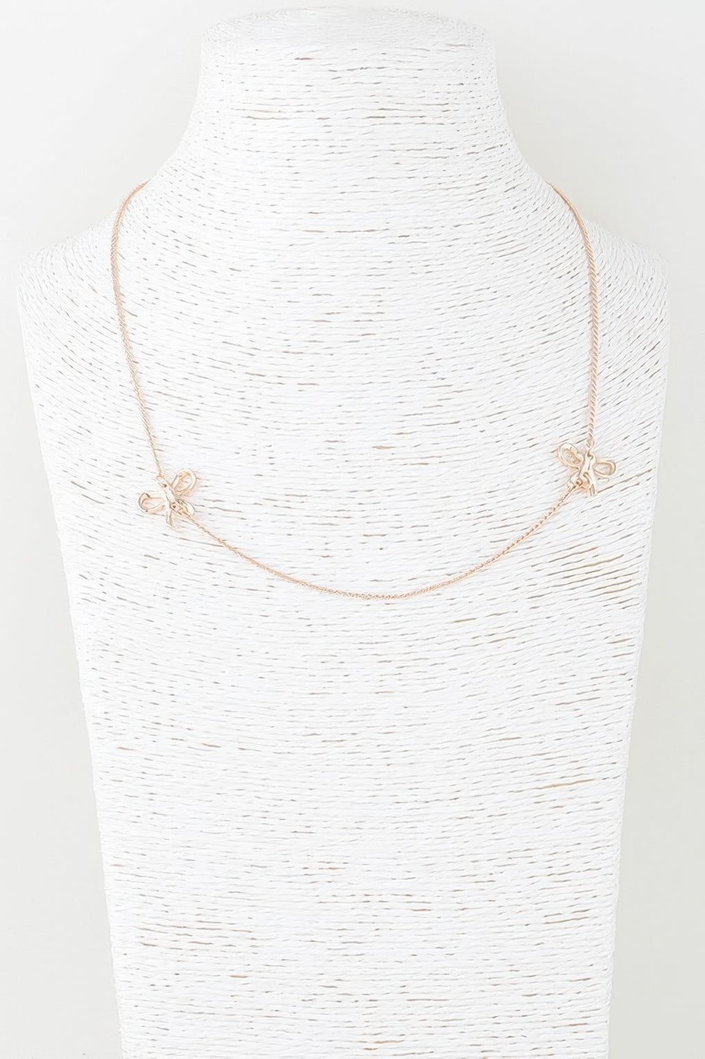 Gold double ribbon chain necklace on bust, bow charms at both sides