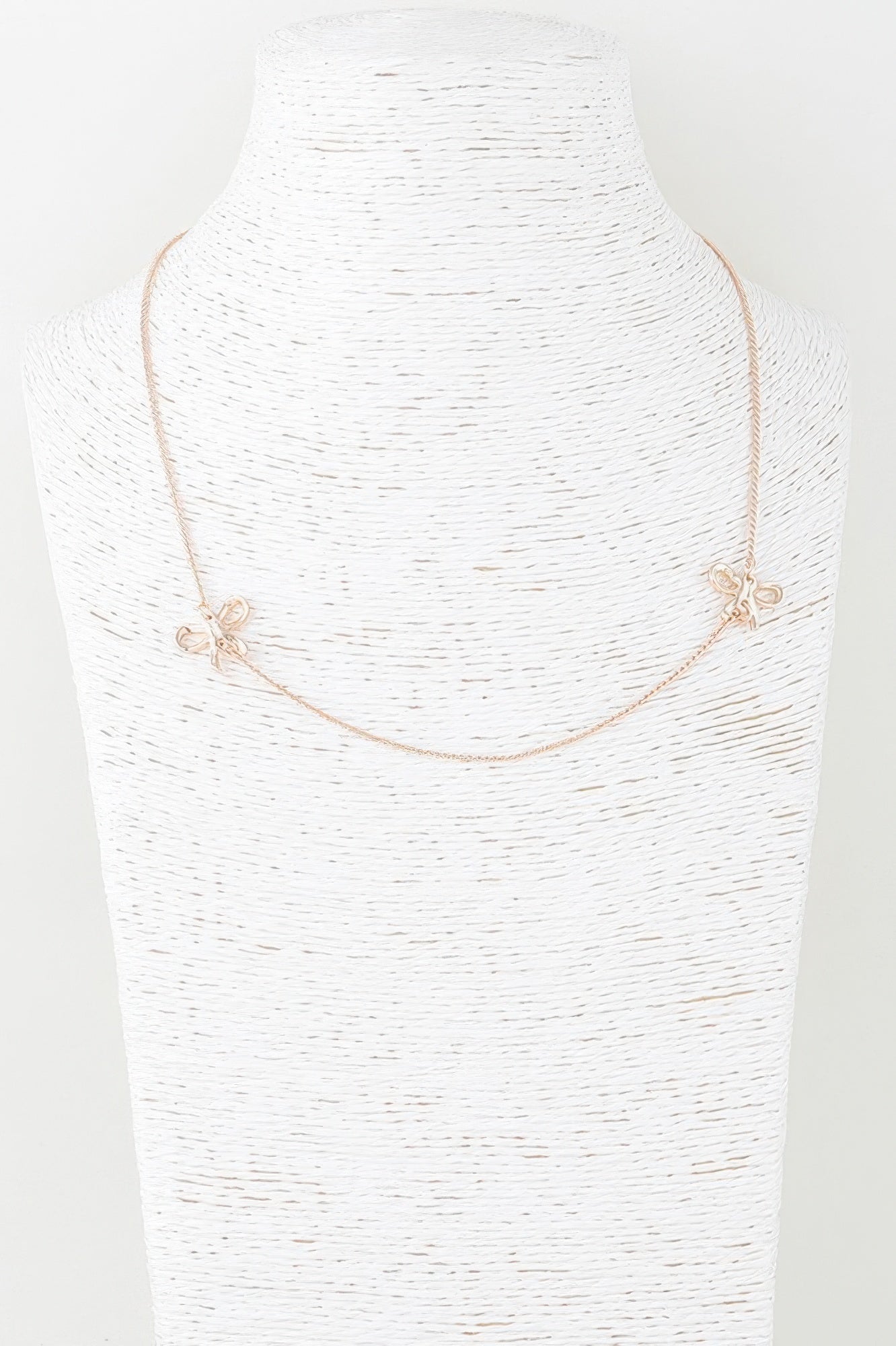 Gold double ribbon chain necklace on bust, bow charms at both sides