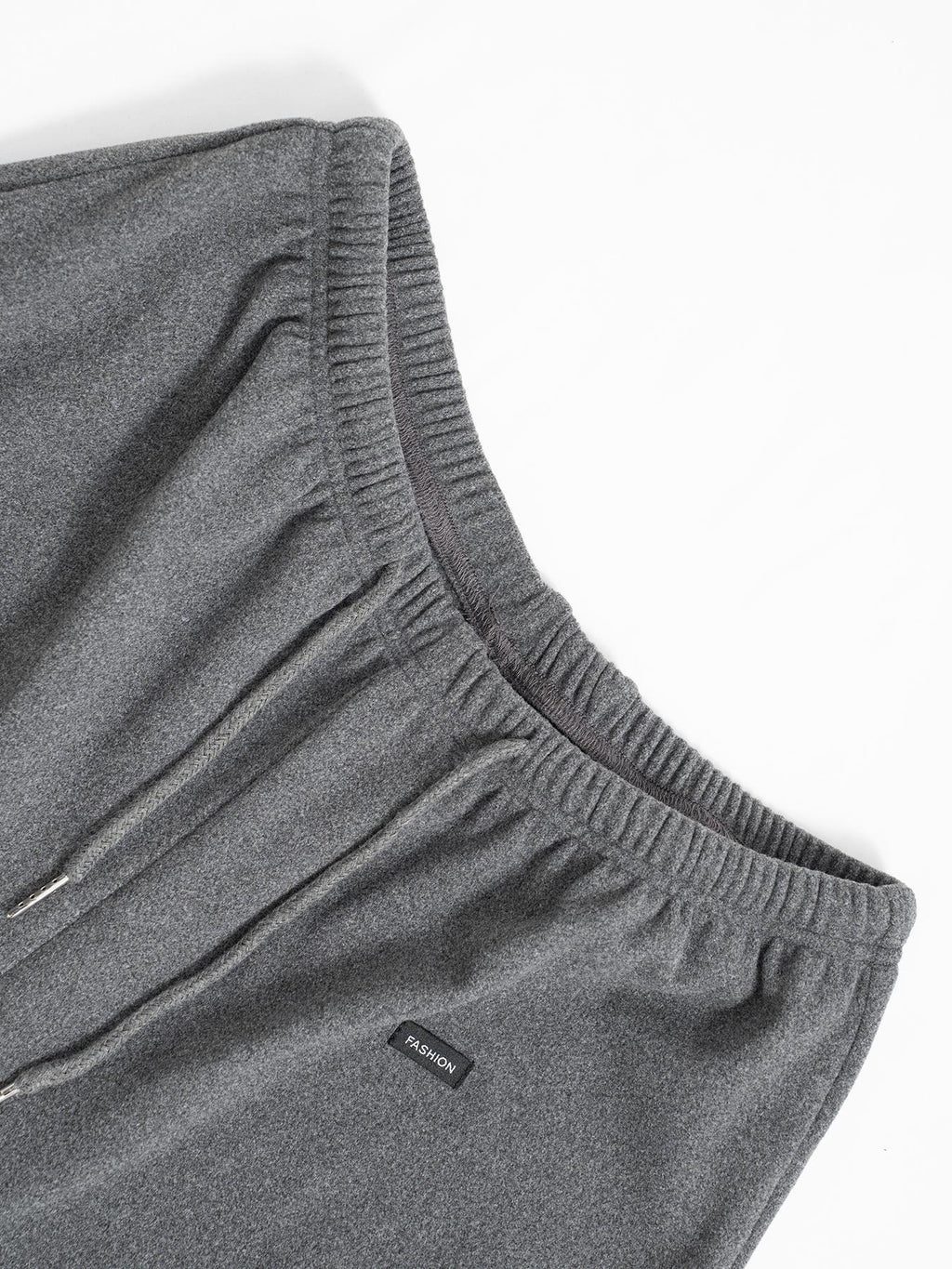 Gray drawstring pants close-up: elastic waistband, drawcord ties, logo patch