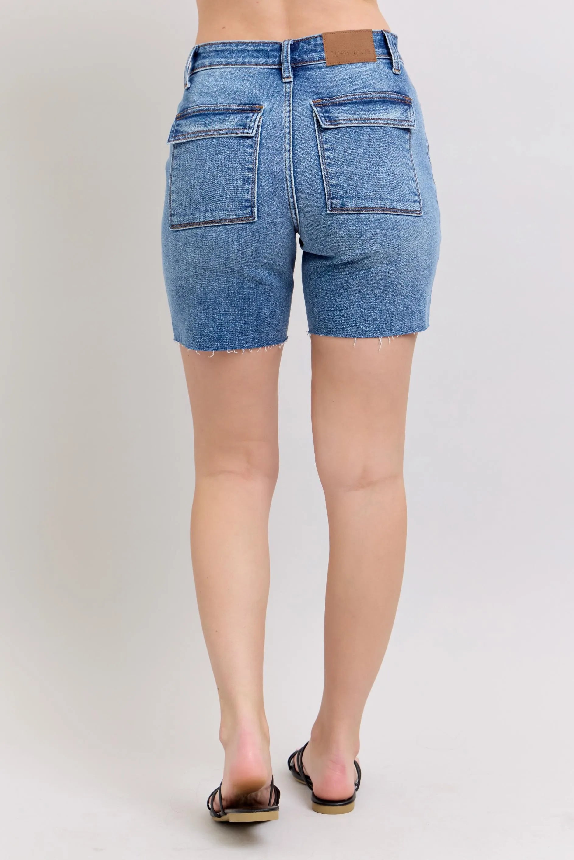 Back view of plus-size denim bermuda shorts, light blue wash, back flap pockets, frayed hem