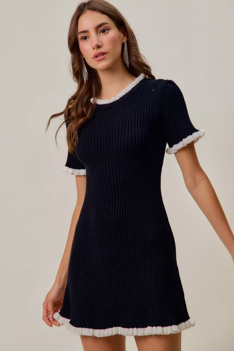 Black ribbed knit mini dress with white ruffle trim at collar, cuffs, and hem